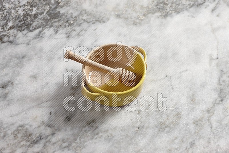 Multicolored Pottery bowl with wooden honey handle in it, on grey marble flooring, 65 degree angle