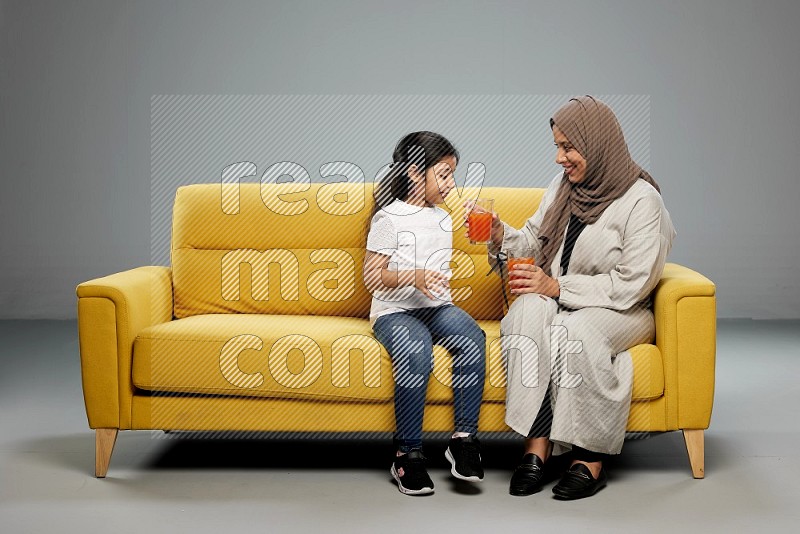 Mom and daughter sitting drinking juice on gray background