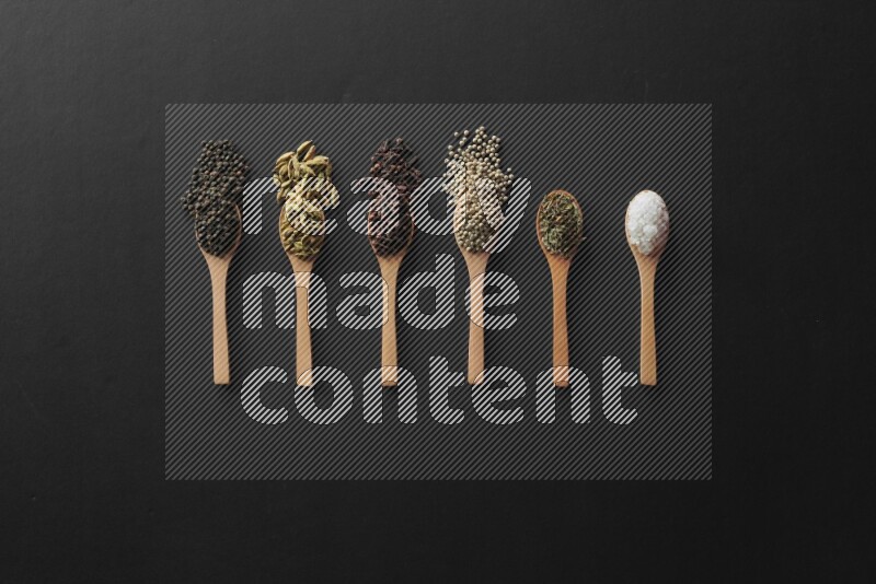 الفلفل الأبيض والقرنفل والهيل والملح والفلفل الأسود وريحان مجفف في معالق خشبية علي خلفية سوداء