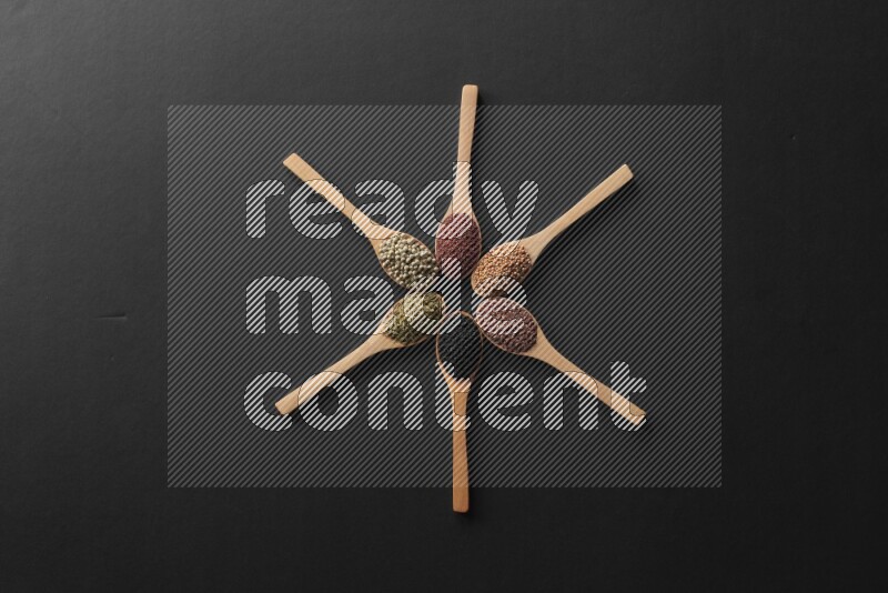 wooden spoons filled with white peppers, mustard seeds, black seeds, garden cress, cumin and flax on black flooring and shaped like a clock
