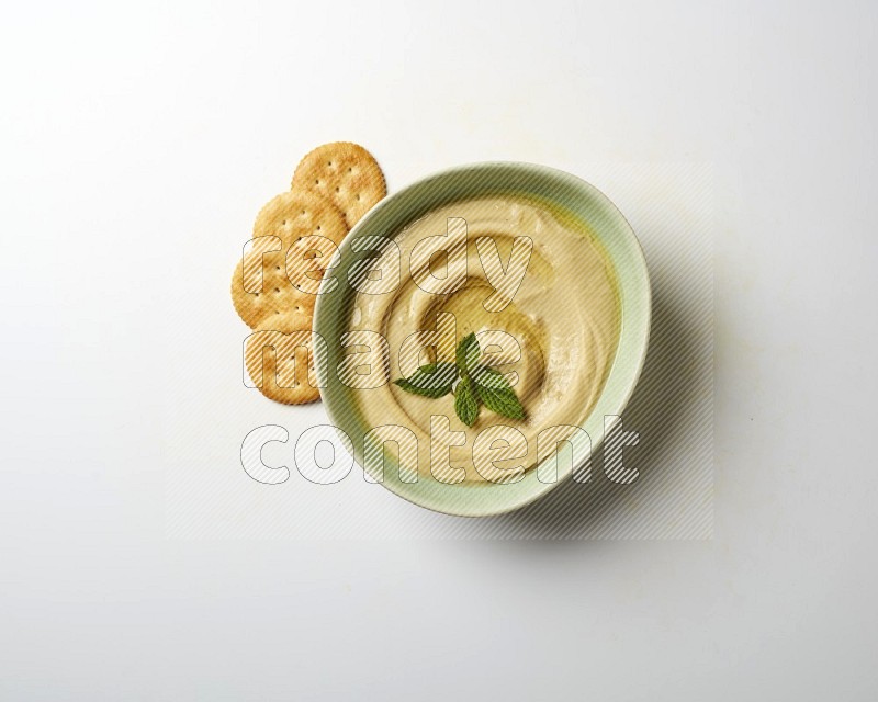 Hummus in a green plate garnished with mint on a white background