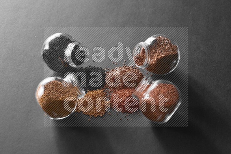 4 glass spice jars full of black seeds, mustard seeds, flax and garden cress on black flooring