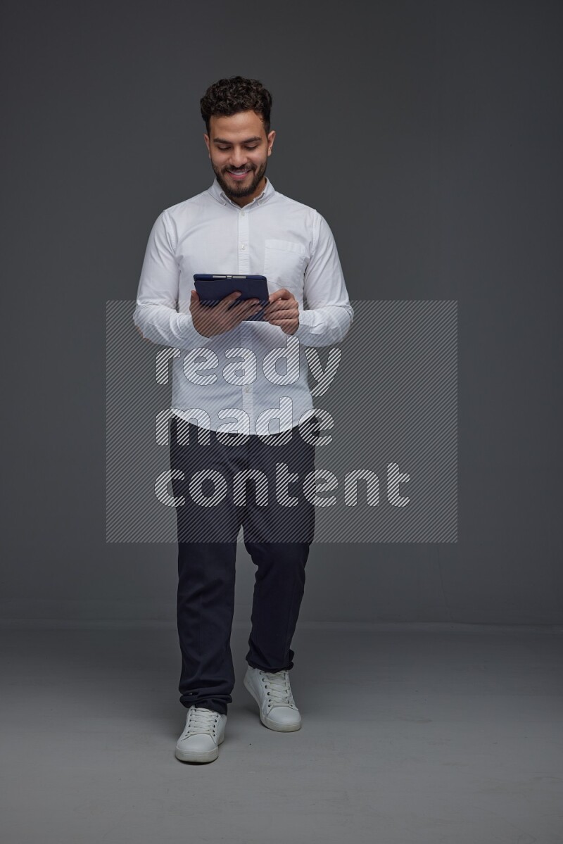 A man wearing smart casual standing and using his tablet eye level on a gray background