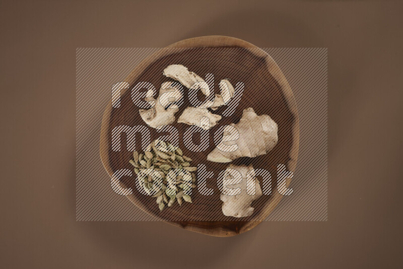 An assorted whole spices on a flat wooden tray including fresh and dried ginger, cinnamon sticks, cardamom, turmeric fingers, cloves, star anise on beige background