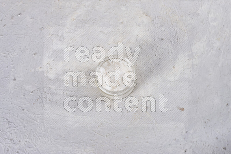 A glass jar full of coarse sea salt crystals on white background