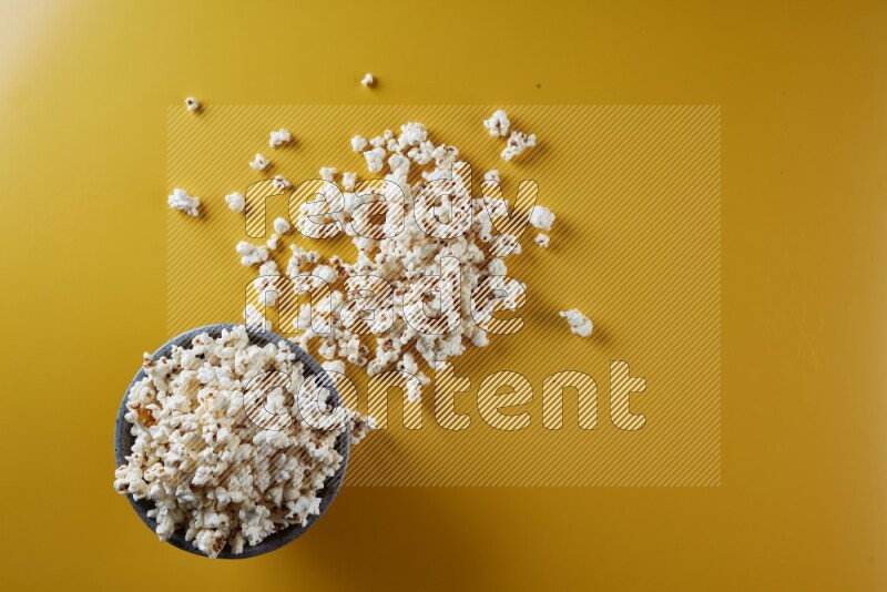 A multicolored pottery bowl full of popcorn with popcorn beside it on a yellow background in different angles