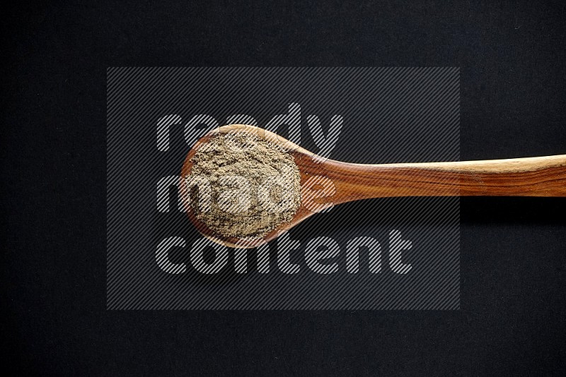 A wooden ladle full of cardamom powder on black flooring