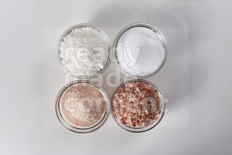 4 glass bowls filled with table salt, coarse sea salt, fine himalayan salt and coarse himalayan salt on white background