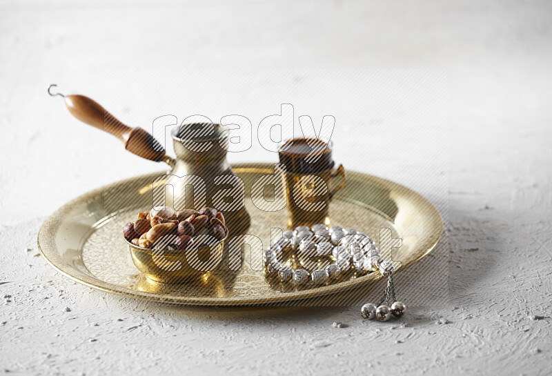 Nuts in a metal bowl with coffee and prayer beads on a tray in a light setup