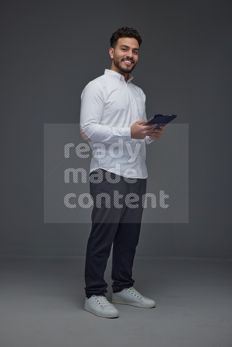 A man wearing smart casual standing and using his tablet eye level on a gray background