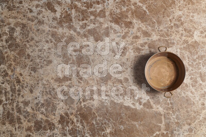 A small copper pan on beige marble background