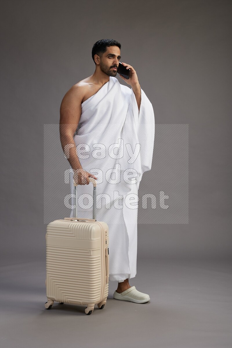 A man wearing Ehram Standing holding traveling bag on gray background