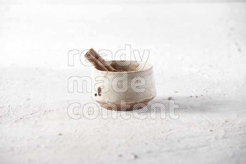 Ceramic beige bowl full of cinnamon powder with a cinnamon stick on a textured white background