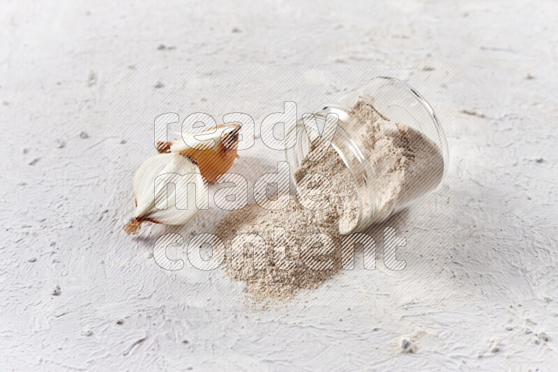 A glass jar full of onion powder flipped with some spilling powder on white background