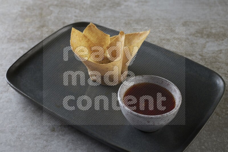 wonton cups with soy sauce ramkin on rectangle dark grey ceramic plate on grey textured counter top