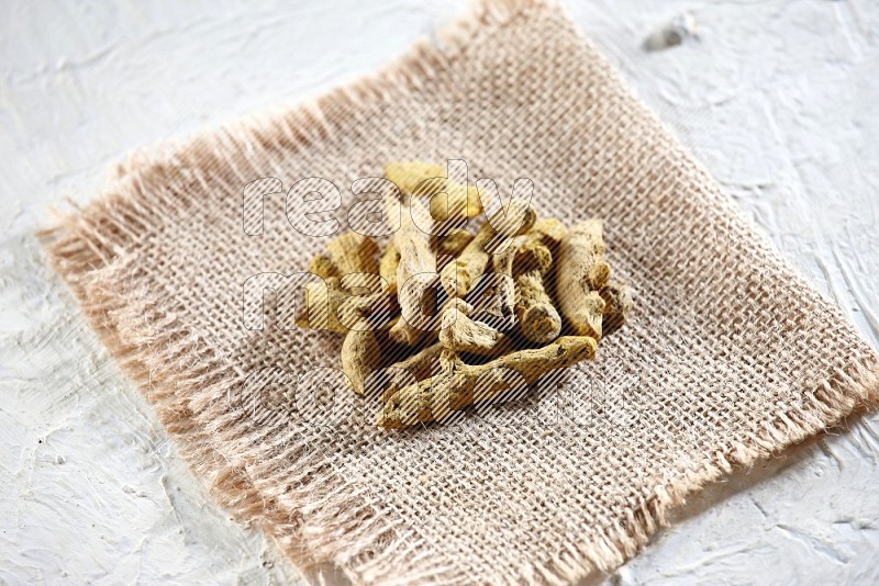 Dried turmeric whole fingers on a piece of burlap on a textured while flooring