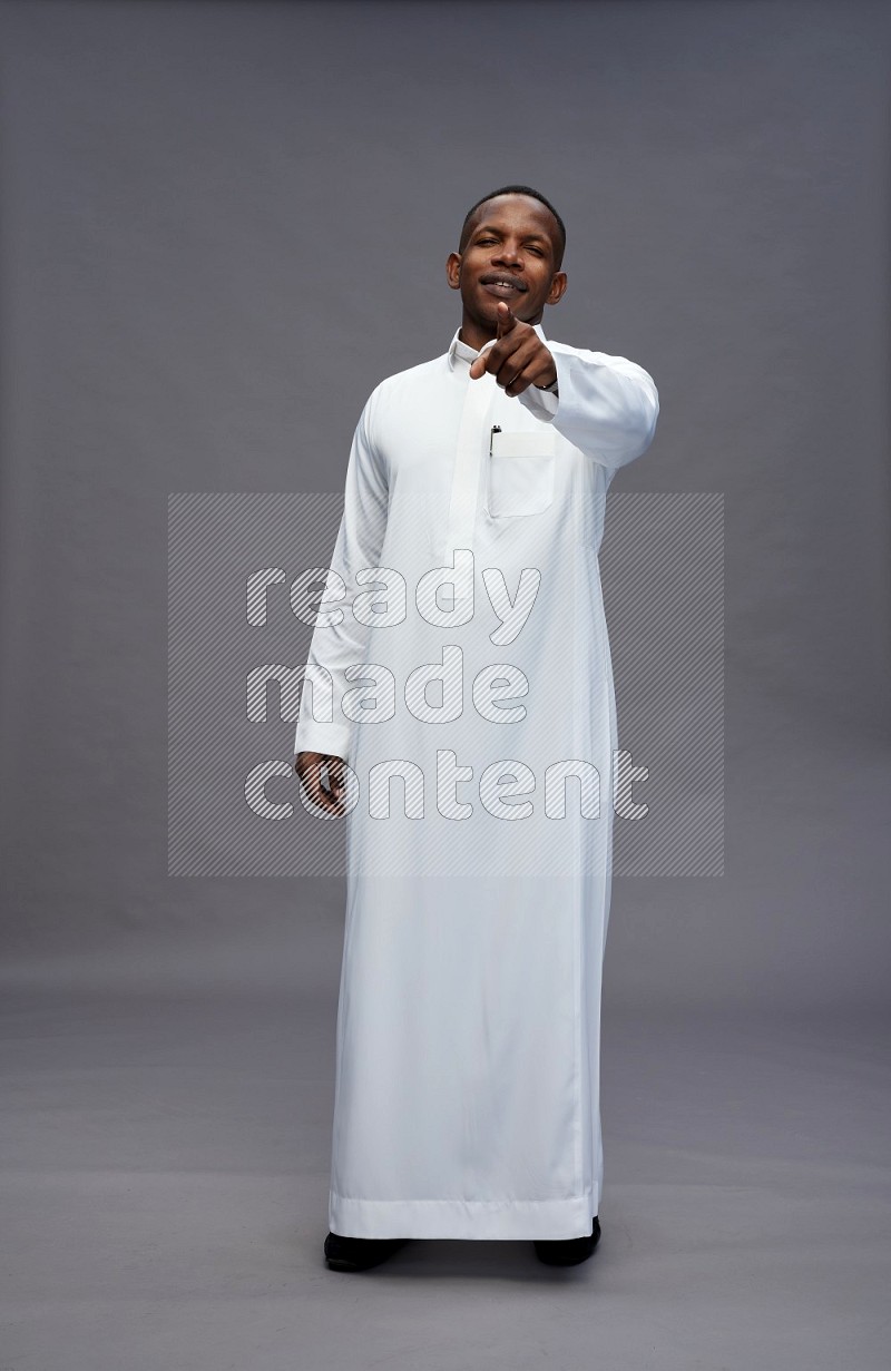 Saudi man wearing thob standing interacting with the camera on gray background