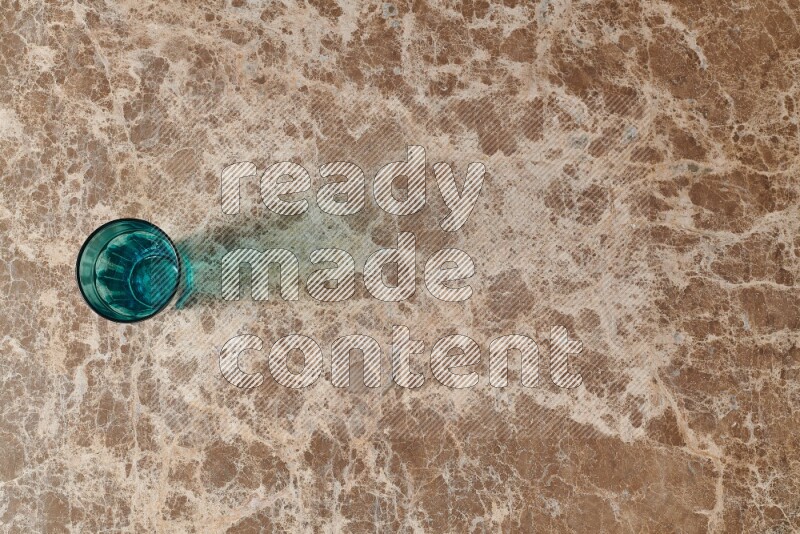 A turquoise glass cup on beige marble background