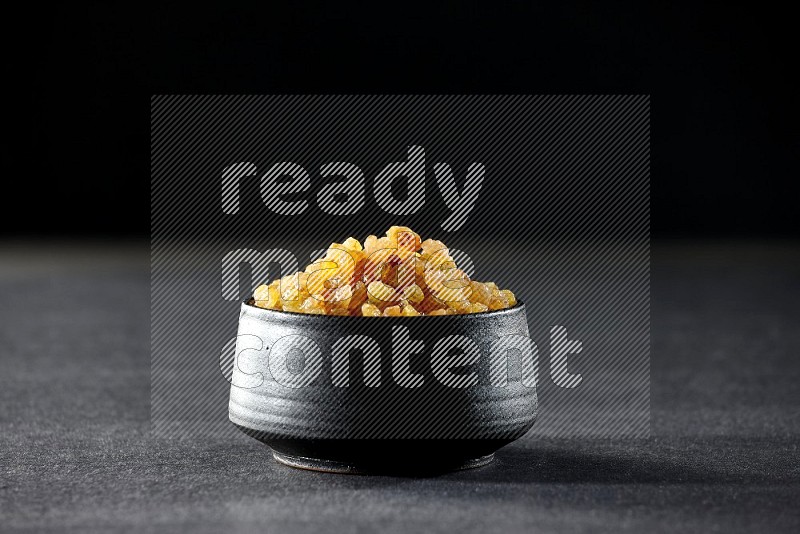 A black pottery bowl full of raisins on a black background in different angles