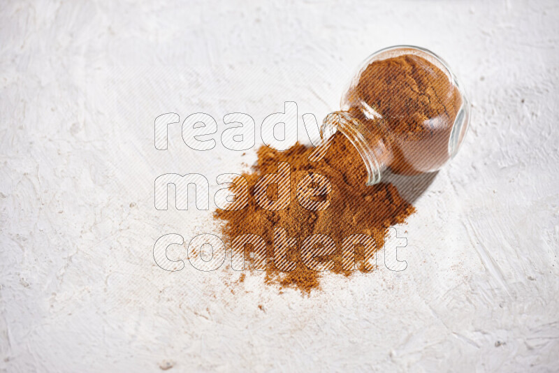 A glass jar full of ground paprika powder flipped with some spilling powder on white background