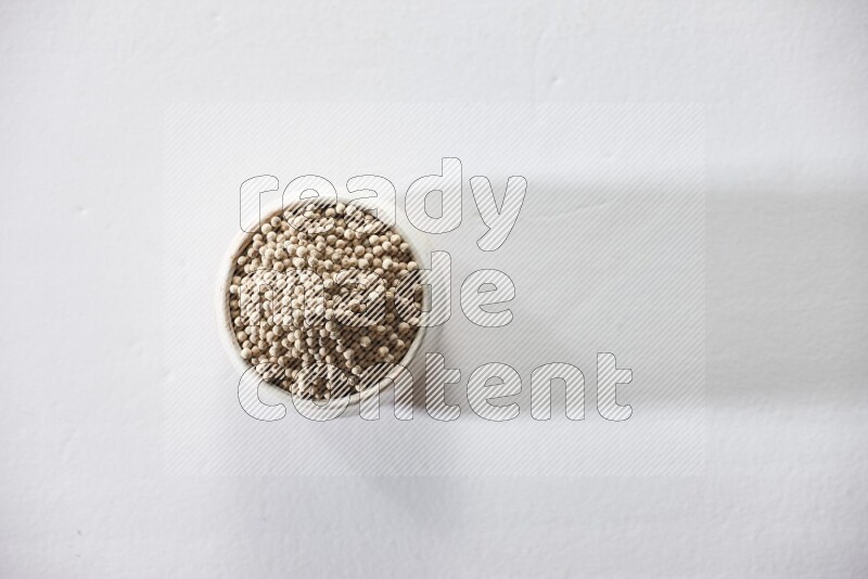 وعاء فخار بيج ممتلئ بحبوب الفلفل الأبيض على أرضية بيضاء