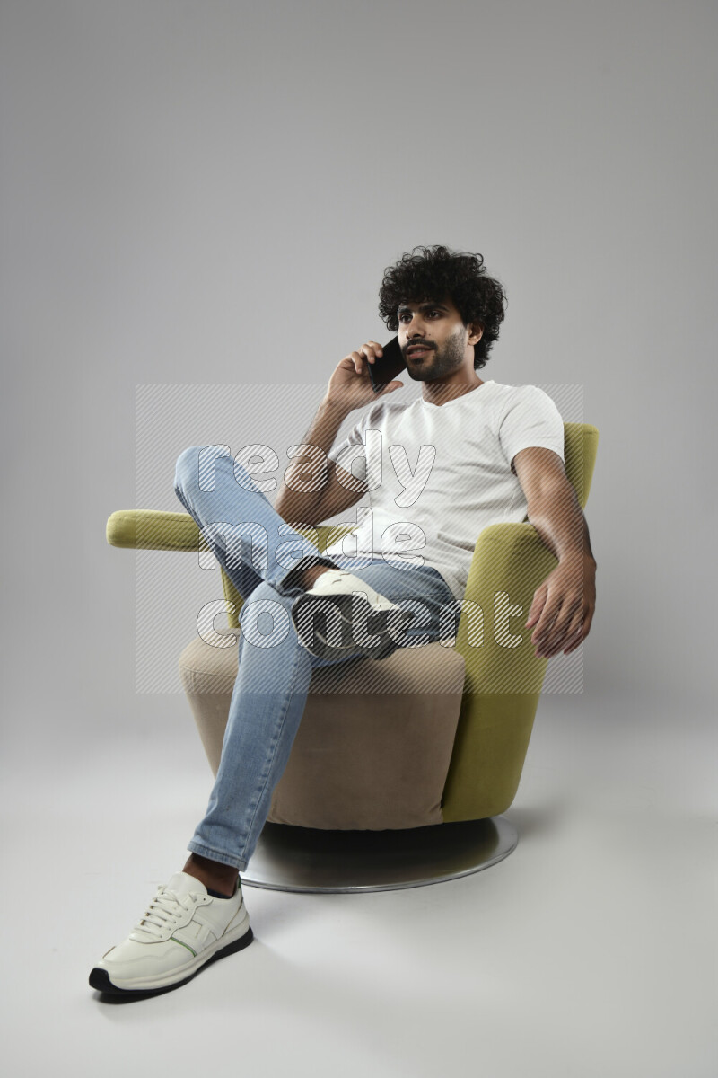A man wearing casual sitting on a chair talking on the phone on white background