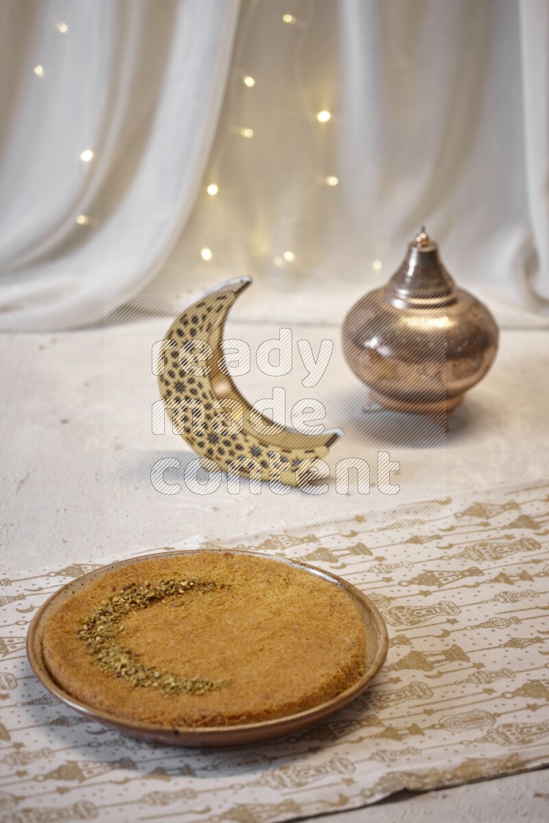 صحن من الكنافة بجانب فوانيس علي خلفية بيضاء خشبية