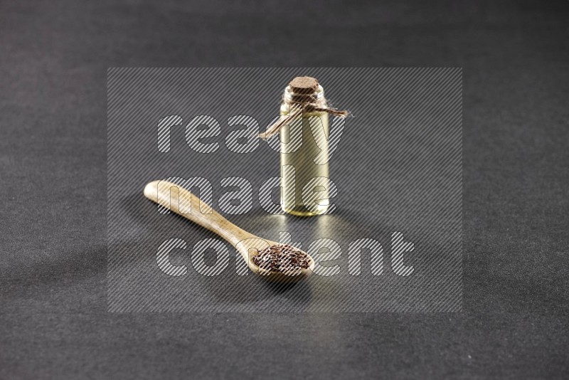 A wooden spoon full of flax and a glass bottle full of flax oil on a black flooring in different angles