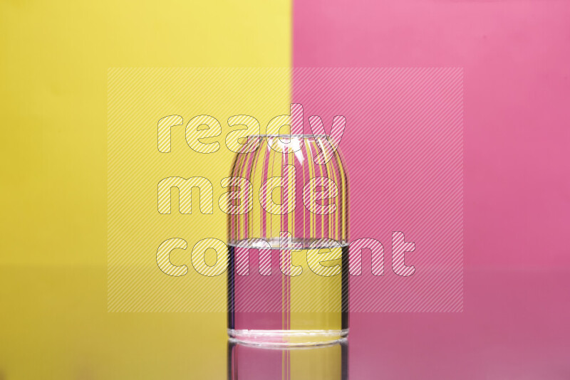 The image features a clear glassware filled with water, set against yellow and pink background
