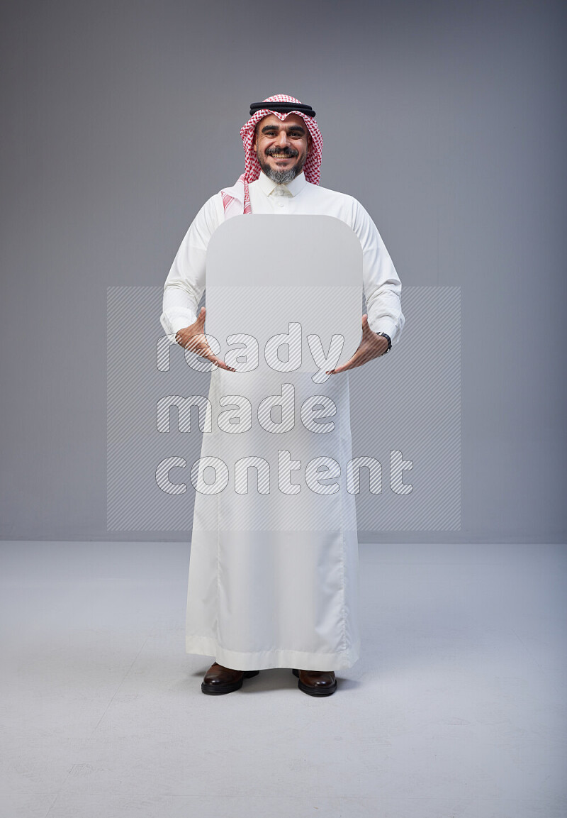 Saudi man Wearing Thob and red Shomag standing holding social media sign on Gray background