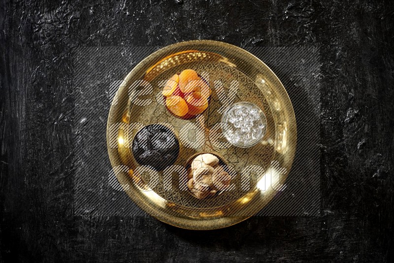 Dried fruits in metal bowls with water on a tray in dark setup