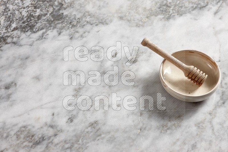 Beige Pottery Bowl with wooden honey handle in it, on grey marble flooring, 65 degree angle