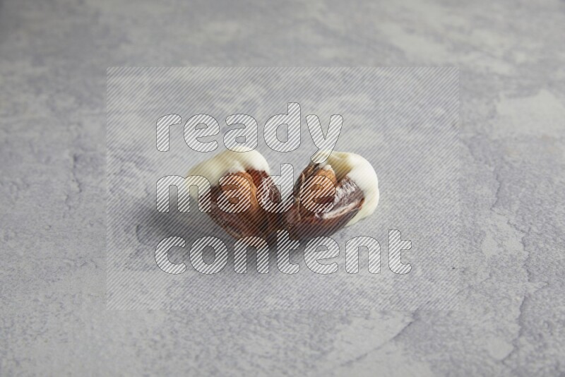 two almonds stuffed dates covered with white chololate on a light grey background