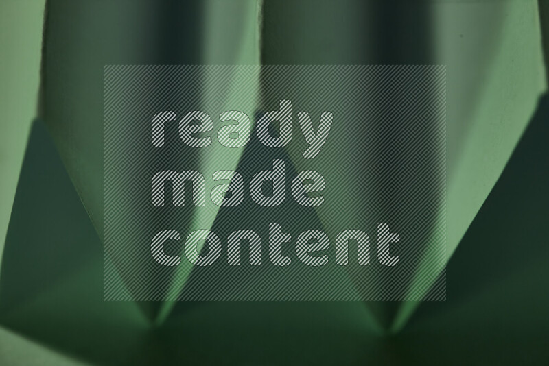 صورة مجردة مقربة تظهر طيات ورقية هندسية حادة بتدرجات اللون الأخضر