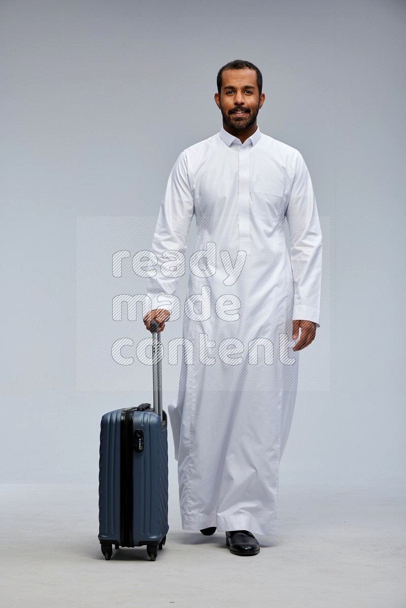 Saudi man wearing thob standing holding Travel bag on Gray background