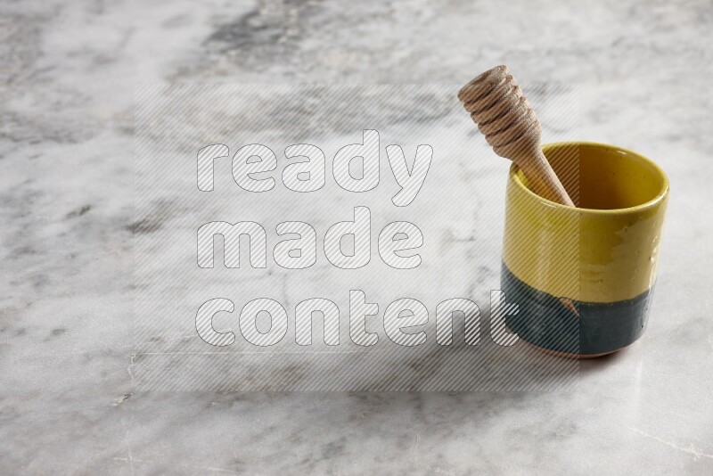 Multicolored pottery cup with wooden honey dipper in it on grey marble background