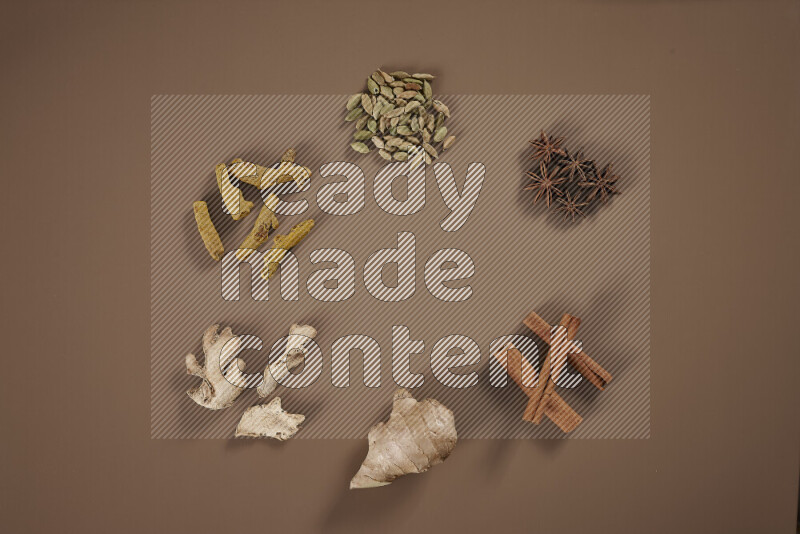 An assorted whole spices including fresh and dried ginger, cinnamon sticks, cardamom, turmeric fingers, cloves, star anise on beige background