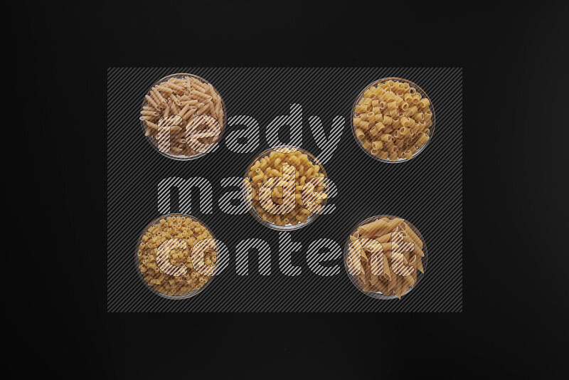 Different pasta types in 5 glass bowls on black background