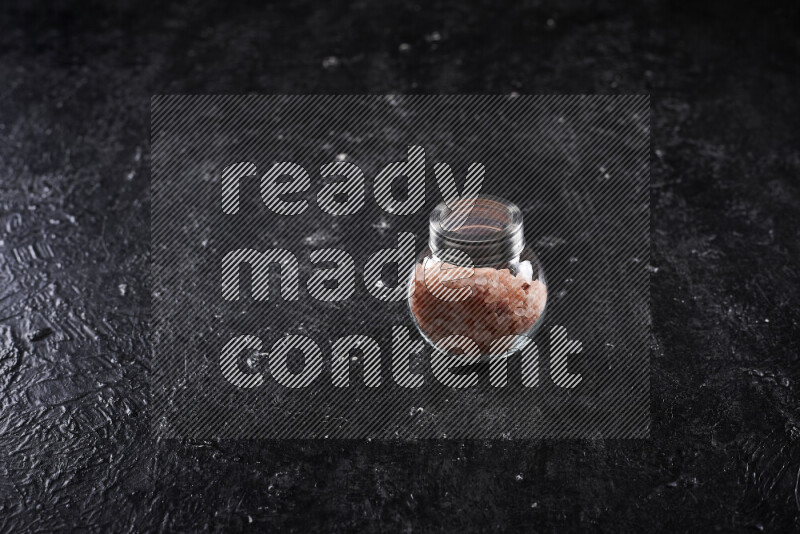 A glass jar full of coarse himalayan salt crystals on black background