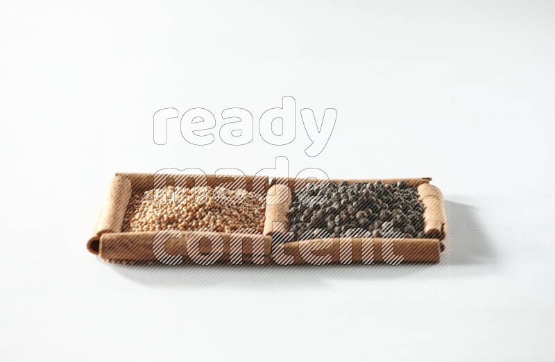 مربعان من أعواد القرفة ممتلئان بحبوب الخردل وحبوب الفلفل الأسود علي خلفية بيضاء