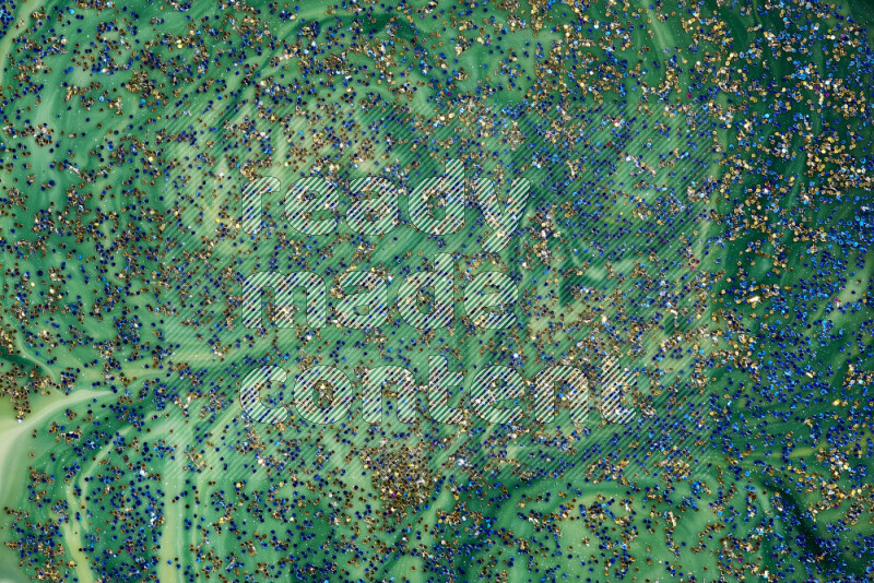 A close-up of sparkling blue glitter scattered on swirling blue and green background