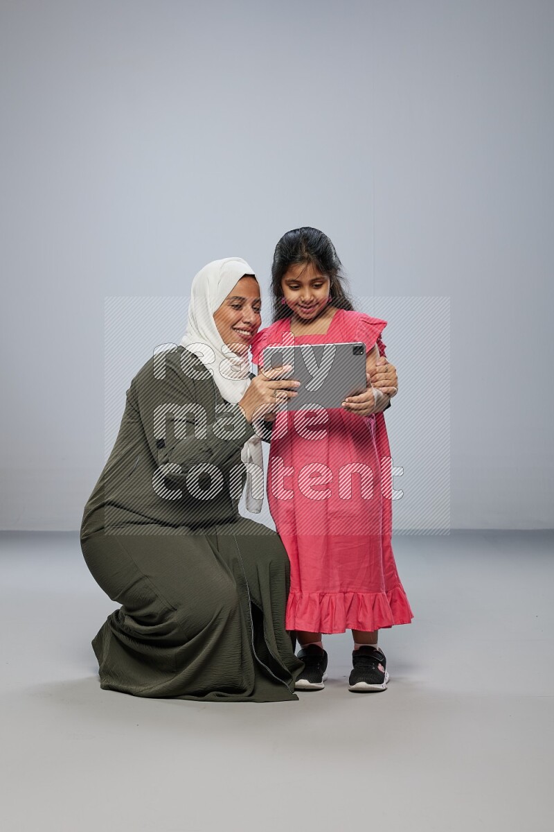 A girl holding an Ipad with her mother on gray background