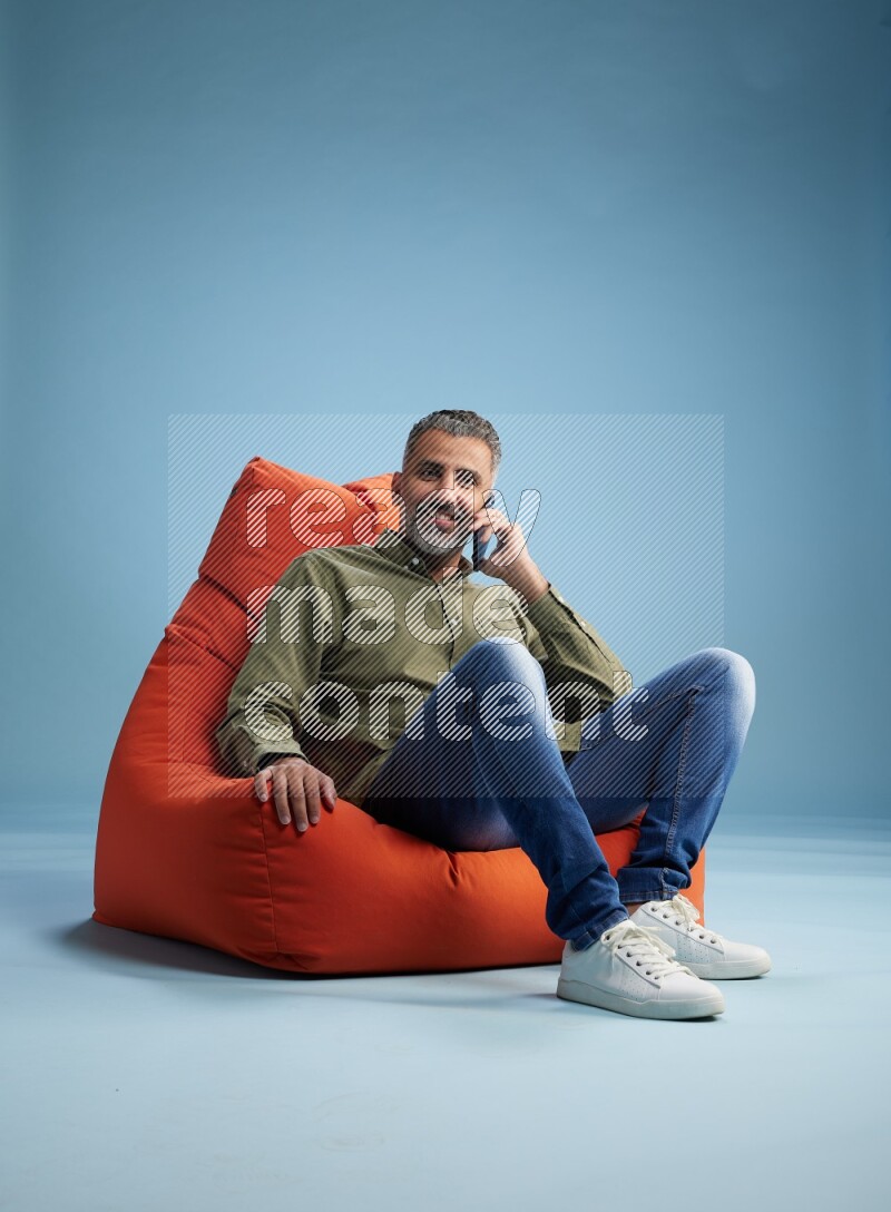 A man sitting on an orange beanbag and talking on the phone