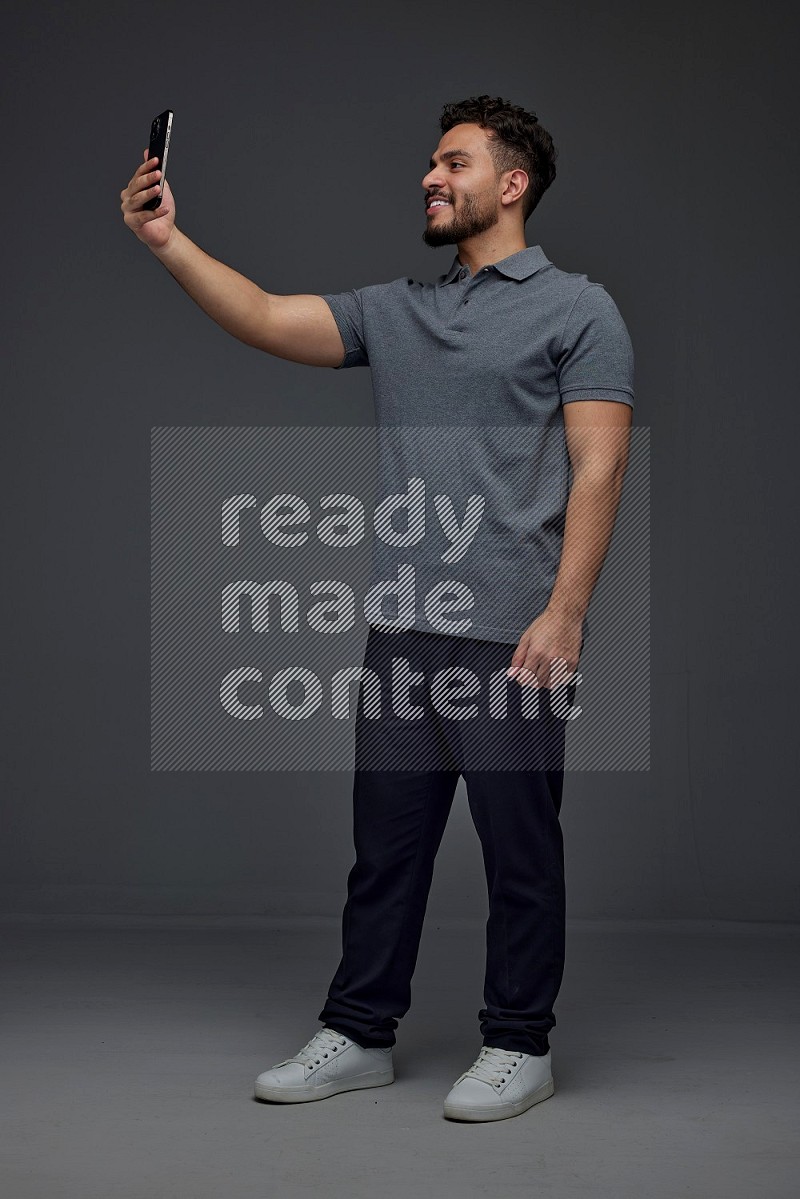 A man wearing casual and taking selfie with his phone different angles eye level on a gray background