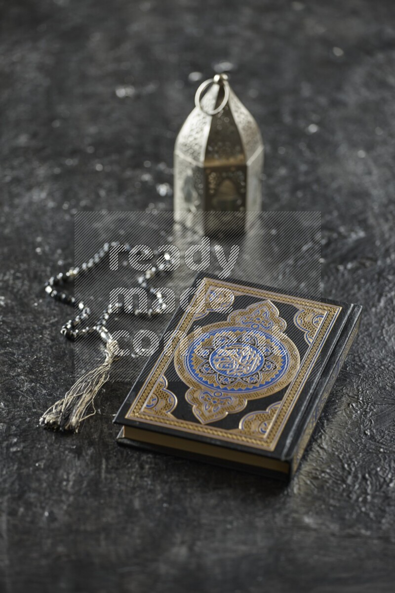 A silver lantern with different drinks, dates, nuts, prayer beads and quran on textured black background