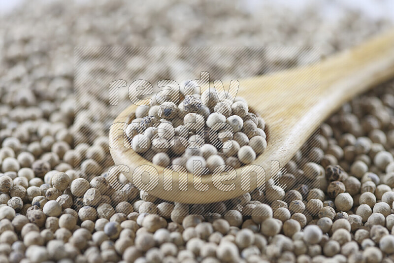 White pepper beads with wooden spoon on white background