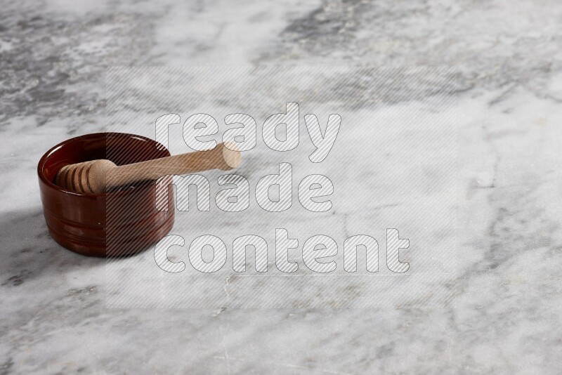 Brown pottery bowl with wooden honey dipper in it on grey marble background