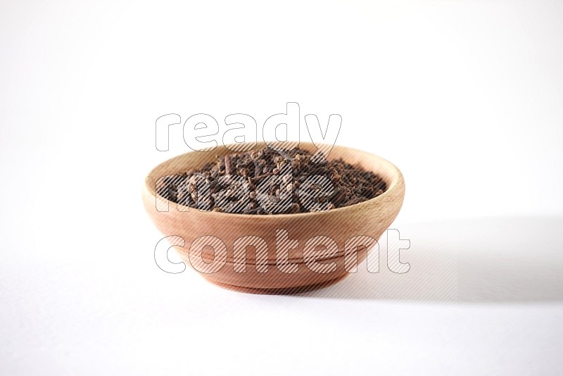 A wooden bowl full of cloves on a white flooring