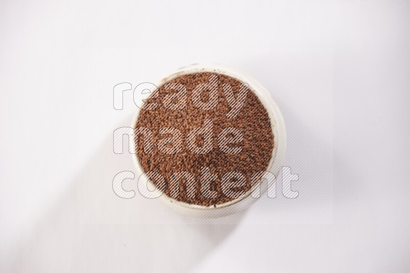 A beige pottery bowl full of garden cress seeds on a white flooring