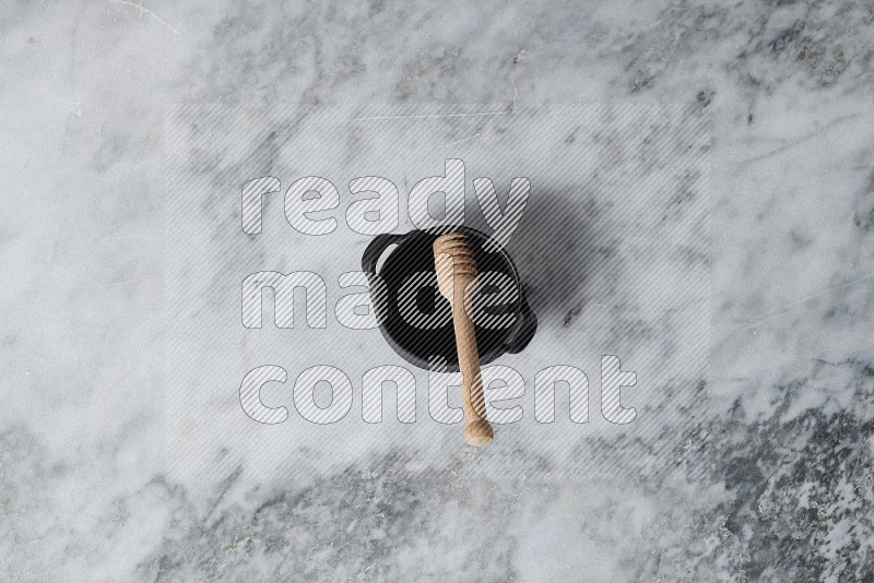 Black Pottery Bowl with wooden honey handle in it, on grey marble flooring, Top View